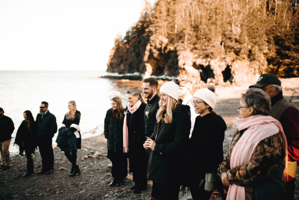 Elopement guests stand on the rocky beach in Owls Head, Maine at golden hour. All guests are smiling and watching the bride and groom say their vows.
Owls Head, Maine elopement. Midcoast Maine wedding photographer. Maine elopement photographer. Maine adventure photographer.