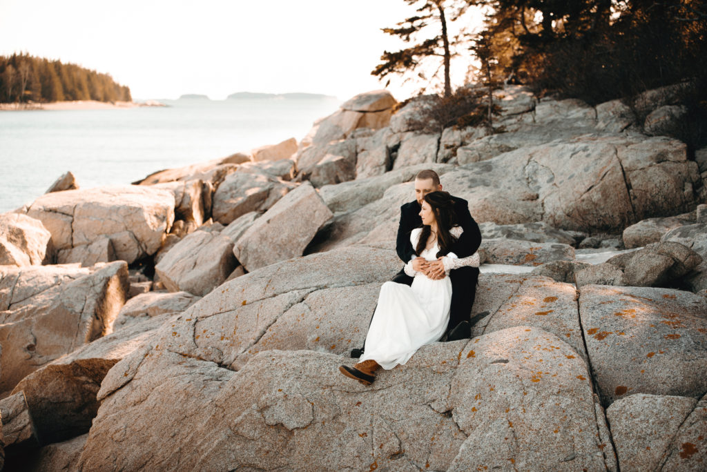 Bride and groom (bride wearing white dress with long lace sleeves and bean boots, groom in black tux) sit snuggled up on the rocks with the ocean behind them in Owls Head, Maine right after saying their private vows for their elopement.
Owls Head, Maine elopement. Midcoast Maine wedding photographer. Maine elopement photographer. Maine adventure photographer.